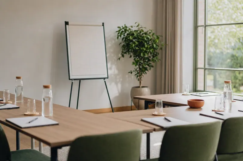 Salle de formation lumineuse, tables disposées en U, blocs-notes et stylos alignés, paperboard vierge et plante verte
